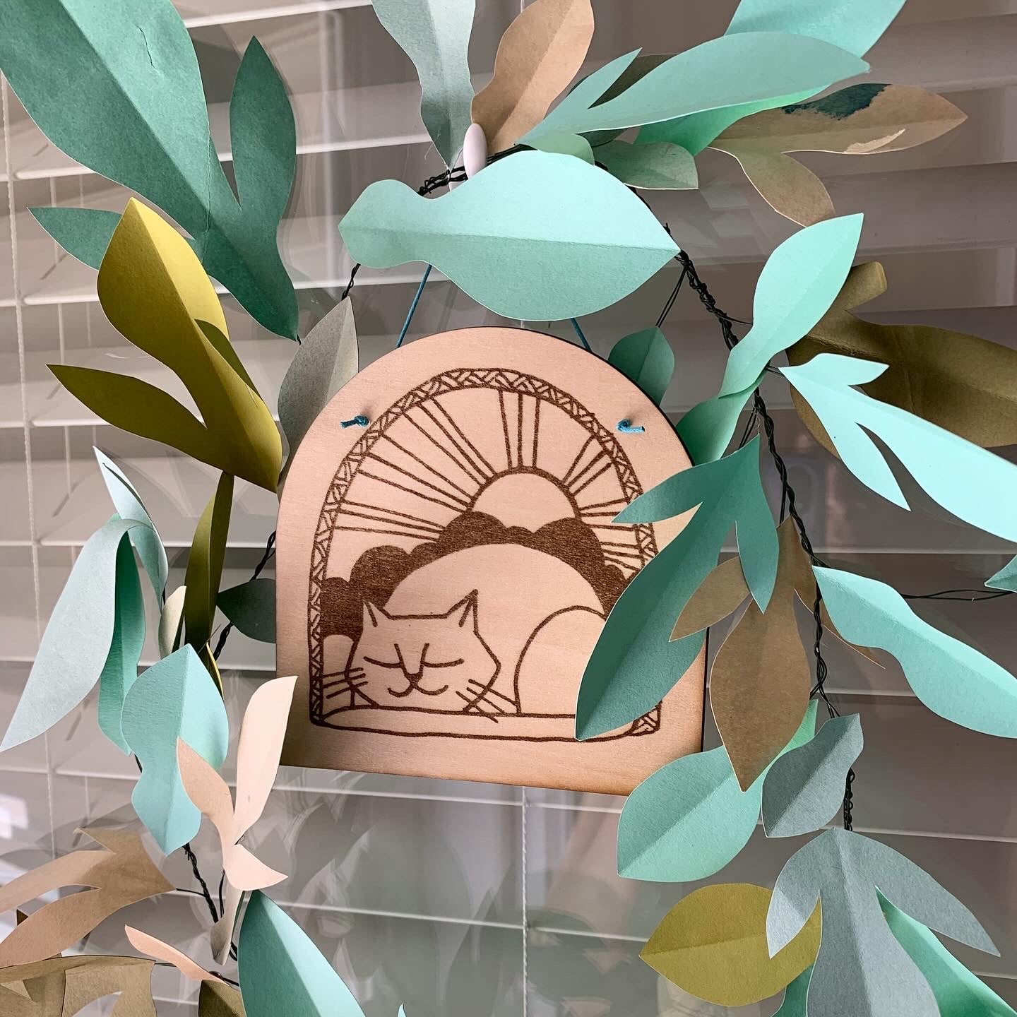 Decorative wall hanging with a cat illustration framed by paper leaves.