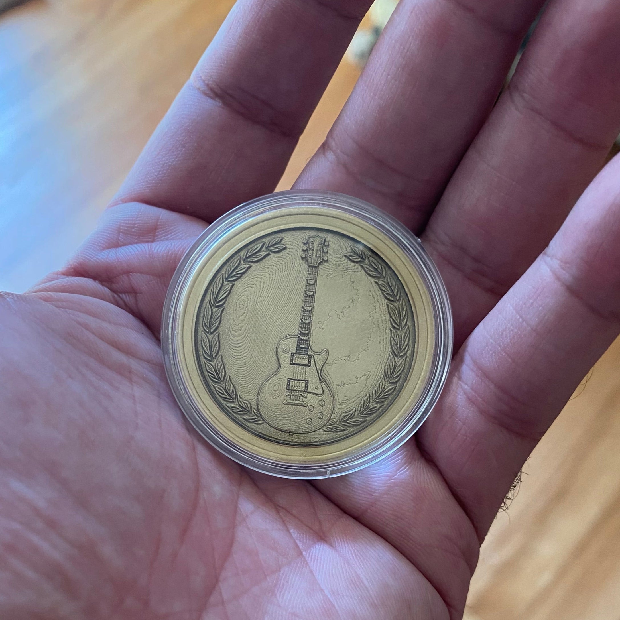 Hand holding a coin with a guitar design on a wooden surface