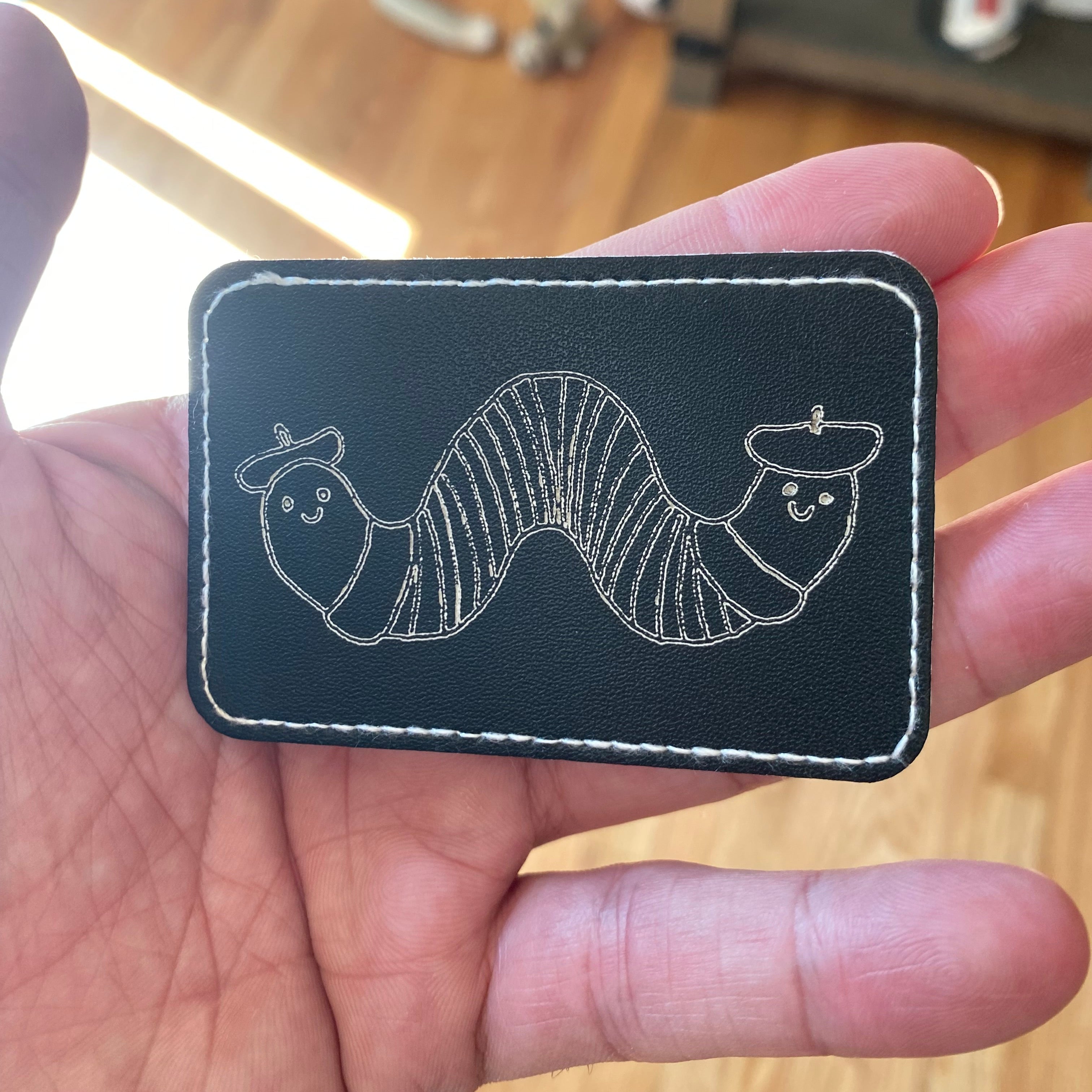 Black patch with white embroidery held in a hand on a blurred background